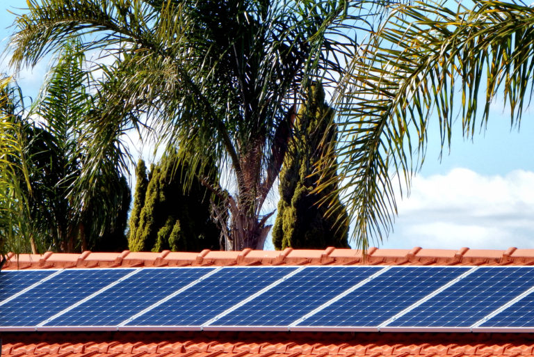 Painéis solares em cima do telhado de uma casa com sistema de energia fotovoltaica instalado e árvores ao fundo.